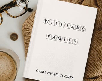 Puede incluir: Cuaderno blanco con las palabras "WILLIAMS FAMILY GAME NIGHT SCORES" impresas en la portada. Las palabras están en fuente negra y están dispuestas en estilo de bloque, como fichas de Scrabble.