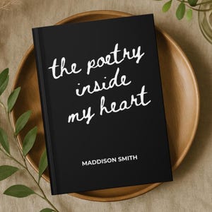 May include: A black journal with the text "the poetry inside my heart" in white script. The author's name, Maddison Smith, is printed below. The journal rests on a wooden plate.
