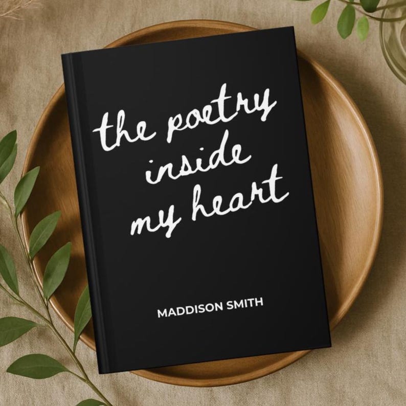 May include: A black journal with the text "the poetry inside my heart" in white script. The author's name, Maddison Smith, is printed below. The journal rests on a wooden plate.
