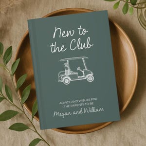 Op de afbeelding: Een hardcover boek met een teal cover, met de tekst "New to the Club" en een witte illustratie van een golfkar. Het boek bevat ook de tekst "Advice and Wishes for the Parents to Be" en de namen "Megan and William".