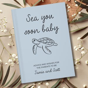 May include: A light blue book with a black line drawing of a sea turtle in the centre. The text reads Sea you soon baby, Advice and wishes for the parents to be, and Jamie and Scott in black lettering on the front cover of the book.