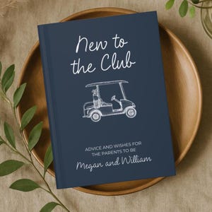 Op de afbeelding: Een marineblauw gastenboek met witte tekst met de tekst "New to the Club" en een schets van een golfkar. De tekst "Advice and Wishes for the Parents to Be" en de namen "Megan and William" zijn ook zichtbaar.