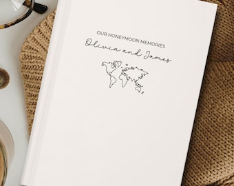 May include: A white hardcover journal with the text "Our Honeymoon Memories Olivia and James" and a simple line drawing of a world map.