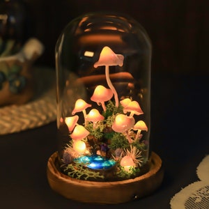 May include: A glass dome with a wooden base containing a miniature forest scene with glowing pink mushrooms and a small blue pond.