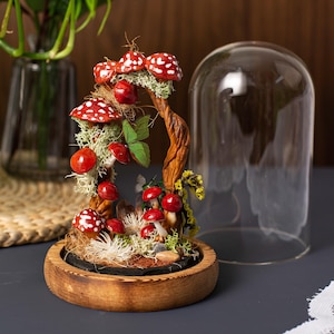 May include: A miniature forest scene with red and white mushrooms, moss, and a twisted branch, all enclosed in a glass dome on a wooden base.