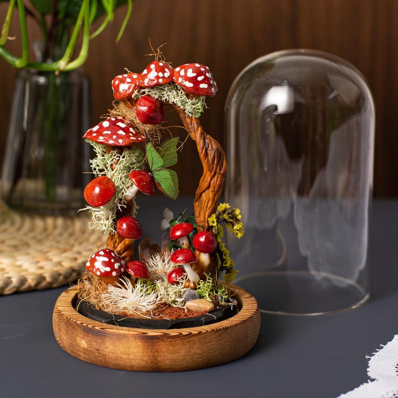 May include: A miniature forest scene with red and white mushrooms, moss, and a twisted branch, all enclosed in a glass dome on a wooden base.
