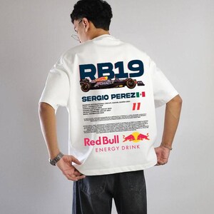 May include: White t-shirt with a Red Bull Racing design. The back shows "RB19" above a race car graphic, the name "SERGIO PEREZ", and the Red Bull logo. Further text provides race details. The shirt is short-sleeved.