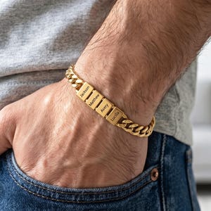 Pode incluir: Uma pulseira de corrente tipo grumet em tom dourado com quatro contas metálicas retangulares, cada uma gravada com um nome: Jackson, Matthew, Avery e Lucilla. A pulseira é composta por elos entrelaçados e repousa sobre um pulso.