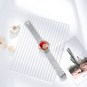 Peut inclure: Une montre en m&eacute;tal argent&eacute; avec un bracelet en maille. Le cadran de la montre pr&eacute;sente une photo d'une jeune fille portant un chapeau rouge.