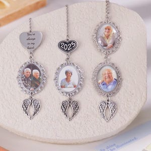 Puede incluir: Tres adornos conmemorativos plateados con fotos de personas mayores. Cada adorno tiene un marco de fotos ovalado, un colgante en forma de coraz&oacute;n con texto y un par de alas de &aacute;ngel. Un adorno tiene el texto "You're always in my heart."