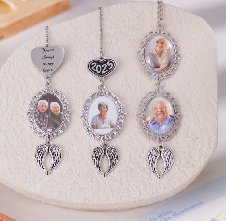 Puede incluir: Tres adornos conmemorativos plateados con fotos de personas mayores. Cada adorno tiene un marco de fotos ovalado, un colgante en forma de coraz&oacute;n con texto y un par de alas de &aacute;ngel. Un adorno tiene el texto "You're always in my heart."