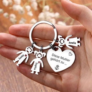 Peut inclure: Porte-cl&eacute;s en argent avec un charme en forme de c&oelig;ur qui dit "Diese Mutter geh&ouml;rt zu..." et quatre charmes en forme de bonhomme allumette avec les noms "Amelia", "Henry", "Sophia" et un c&oelig;ur.