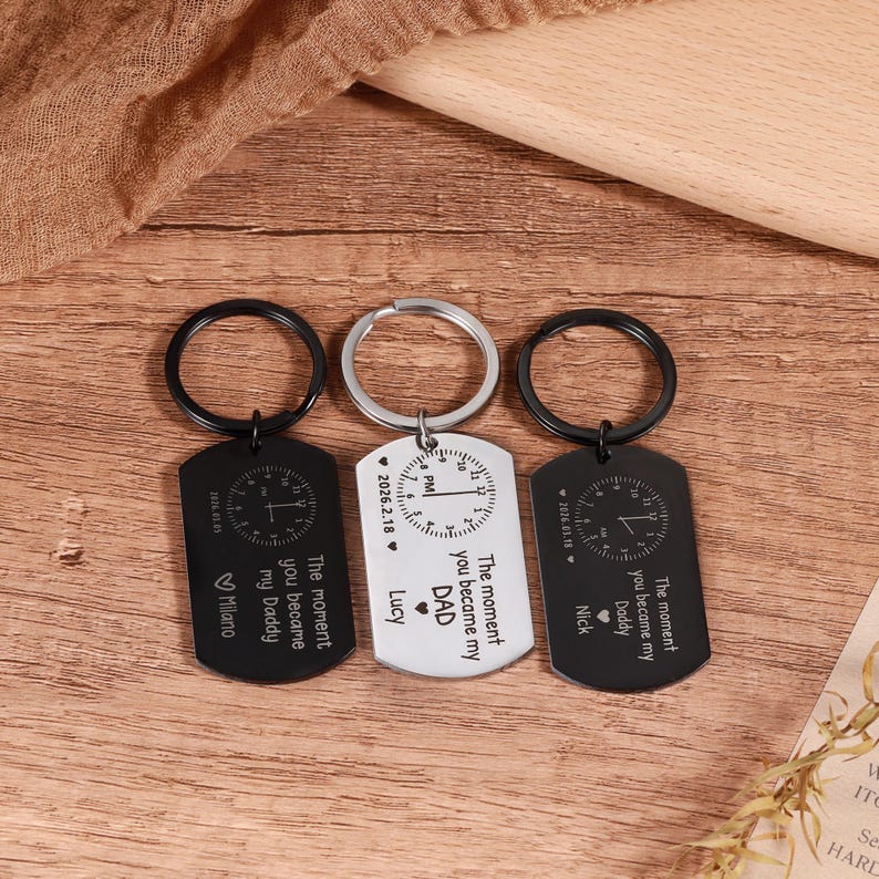 May include: Three dog tag keychains with black and silver finishes. Each tag features a clock design and the text "The moment you became my Daddy" or "DAD". The keychains include names like "Nick", "Lucy", and "Milano".