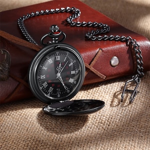 May include: A black pocket watch with a black chain. The watch face has Roman numerals and a black background with red accents. The watch is open and the back is visible.