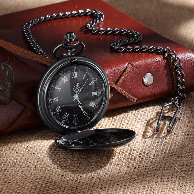 May include: A black pocket watch with a black chain. The watch face has Roman numerals and a black background with red accents. The watch is open and the back is visible.
