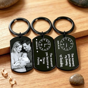 May include: Three black keychains with black rings. One keychain features a black and white photo of a family. The other two keychains have a clock design and the text "The moment you became us Three Paisley" and "The moment you became my Daddy Rosalina".
