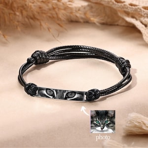 Könnte beinhalten: Schwarzes geflochtenes Armband mit einem rechteckigen Silberanhänger, der Katzenaugen zeigt. Der Anhänger ist mit einem Foto einer Katze mit grünen Augen personalisiert.