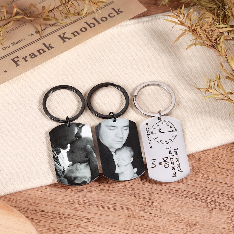 May include: Three personalized dog tag keychains. Two tags feature black and white photos, while the third has a clock design and the text "The moment you became my DAD". Each keychain has a metal ring.