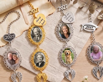 May include: Four hanging memorial ornaments with metal chains, each featuring oval photo frames, angel wing charms, and 2027 year tags. Two ornaments are gold-toned and two are silver-toned, with heart-shaped charms inscribed with Always in my heart.