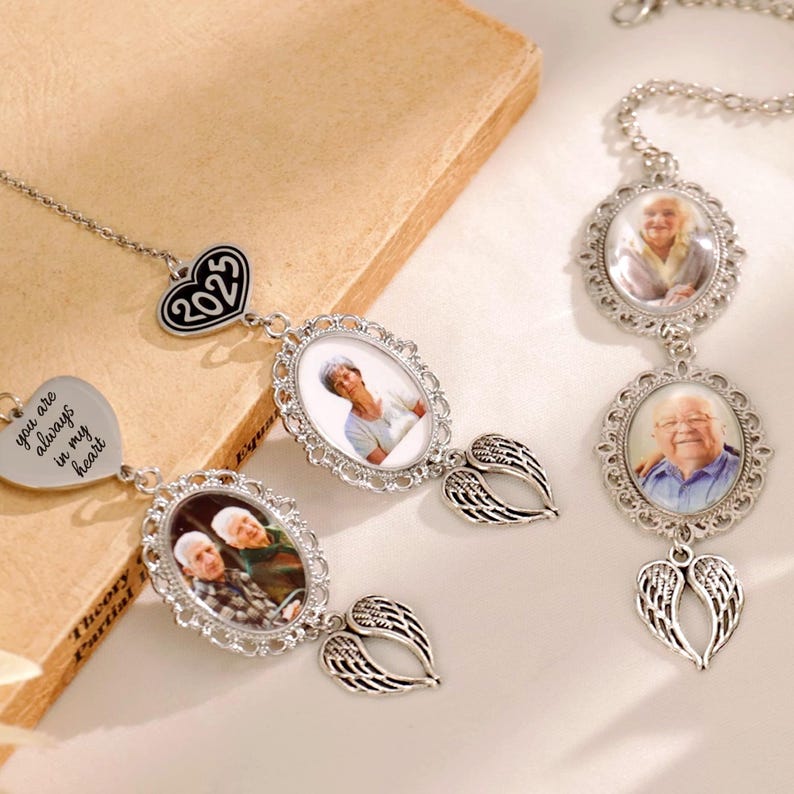 Puede incluir: Colgantes conmemorativos plateados con marcos de fotos ovalados, alas de &aacute;ngel y dijes en forma de coraz&oacute;n. Un dije dice "you are always in my heart", otro tiene "2023". Los colgantes contienen fotos de personas.