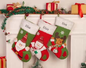 May include: Three personalized Christmas stockings with green and red fabric. The stockings feature a snowman, a reindeer, and Santa Claus. The stockings are hung on a white fireplace mantel with a green garland.