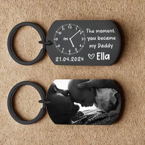 May include: Black keychain with a clock design and the text "The moment you became my Daddy" and the name "Ella". The second keychain has a black and white photo of a baby and a person.