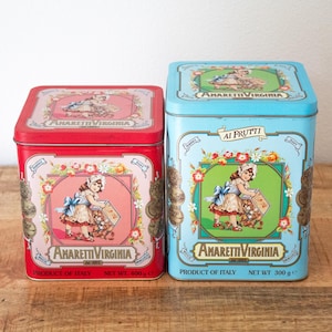 May include: A red square tin labelled Amaretti Virginia with a net weight of 400g and a light blue square tin labelled Amaretti Virginia Ai Frutti with a net weight of 300g. Both tins feature a graphic of a child and floral border designs.