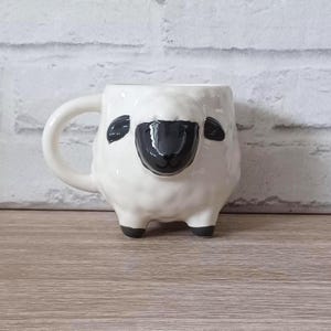 May include: A novelty sheep-shaped mug. The white ceramic mug features a black face and ears, with a handle and four black feet. This quirky mug is a fun addition to any kitchen, perfect for tea or coffee.