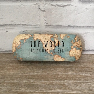 Pode incluir: Um estojo para óculos azul e marrom com um design de mapa mundial vintage. O estojo tem o texto "The World Is Yours To See" impresso nele.