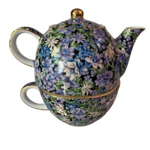 Könnte beinhalten: Eine schwarz-weiße Teekanne mit einem Blumenmuster in Blautönen und Lila. Die Teekanne hat einen goldenen Rand und eine passende Tasse.