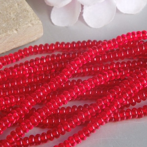May include: A strand of bright red glass seed beads. The beads are small and round, and they are arranged in a loose pile.