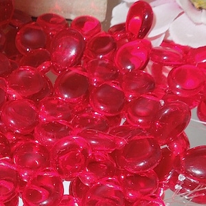 May include: A large group of bright red glass pebbles. The pebbles are smooth and round, and they are all about the same size.
