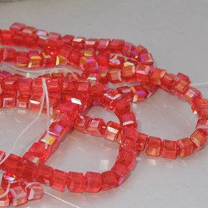 May include: Strands of vibrant red, faceted cube beads strung on white thread. The beads have an iridescent quality, reflecting multiple colors. These beads are suitable for jewelry making and craft projects.
