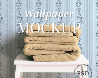 May include: A stack of folded beige towels on a white stool, set against a light blue wallpaper with a floral and striped pattern. The text "Wallpaper MOCKUP" is overlaid on the image.