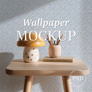 Puede incluir: Una mesa de madera clara con una lámpara en forma de seta con sombrero amarillo y pie blanco, un portalápices beige con lápices de colores y un libro titulado COLORING BOOK LEVEL 1, sobre un fondo de papel pintado con motivos de hojas azules.