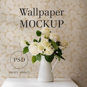 Puede incluir: Una jarra de cerámica blanca llena de hortensias blancas se encuentra sobre una mesa blanca frente a un papel tapiz beige con un patrón floral blanco. El texto "Wallpaper MOCKUP" está en la parte superior de la imagen y "PSD smart object" está en la parte inferior.