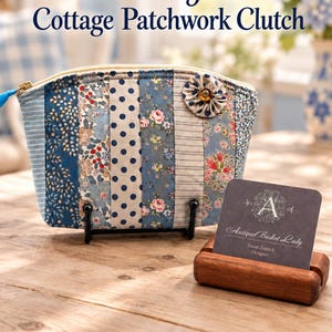 May include: A patchwork clutch featuring vertical fabric strips in various blue, white, and floral patterns, accented with a fabric flower and a gold zipper. A business card for Antique Basket Lady is displayed in a wooden holder next to the clutch.