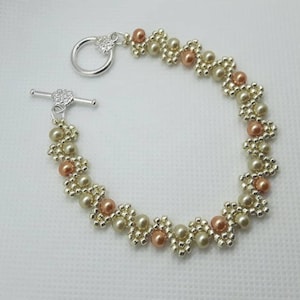 May include: A delicate bracelet made with small, light brown and gold beads, featuring a silver toggle clasp.
