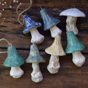 May include: A collection of eight ceramic mushroom ornaments in various shades of blue, green, and yellow. Each mushroom has a white stem and a speckled glaze.