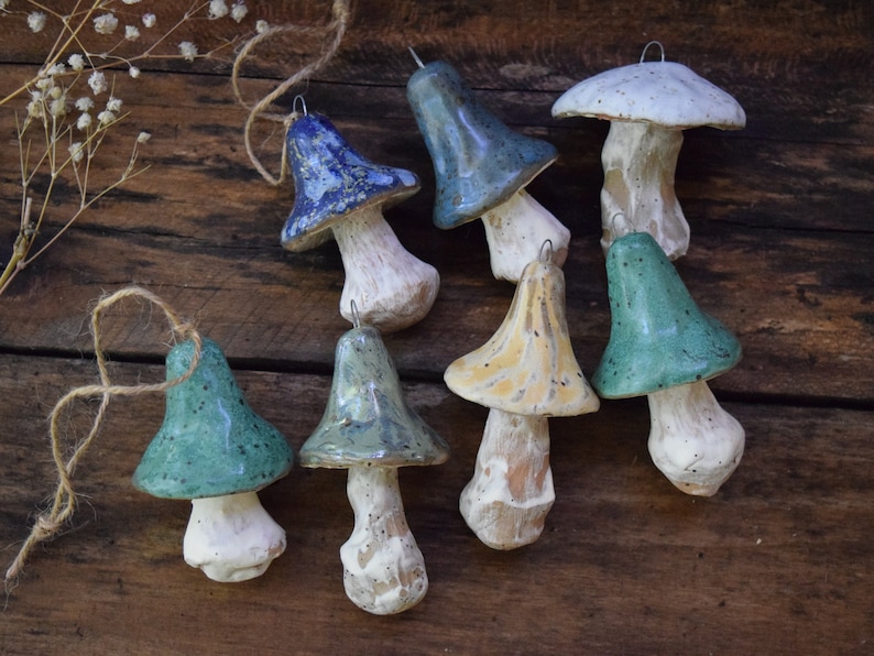 May include: A collection of eight ceramic mushroom ornaments in various shades of blue, green, and yellow. Each mushroom has a white stem and a speckled glaze.