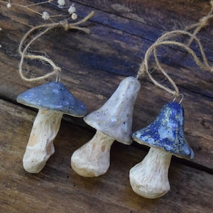 May include: Three ceramic mushroom ornaments with blue and white speckled paint. Each ornament has a string loop for hanging.
