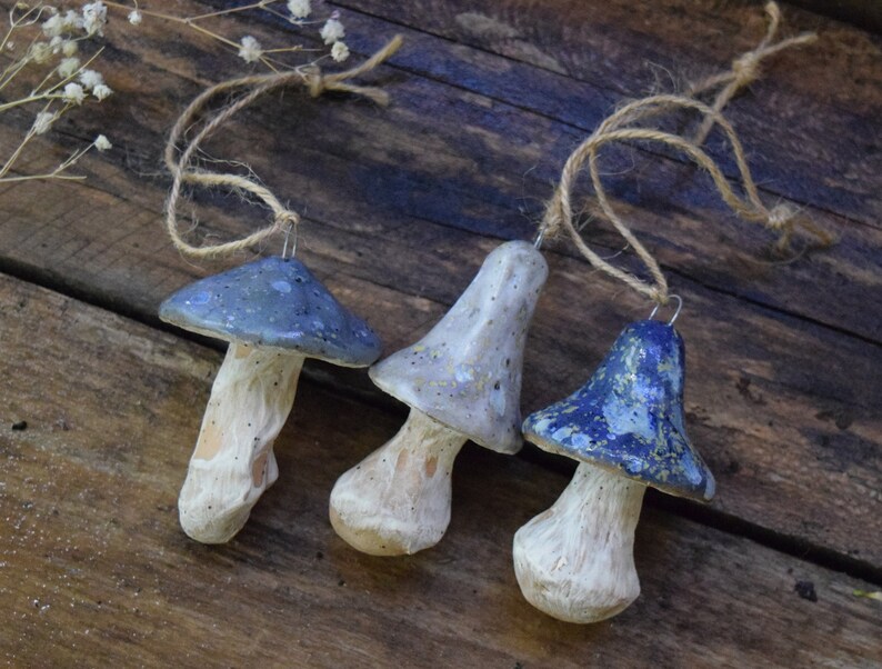 May include: Three ceramic mushroom ornaments with blue and white speckled paint. Each ornament has a string loop for hanging.