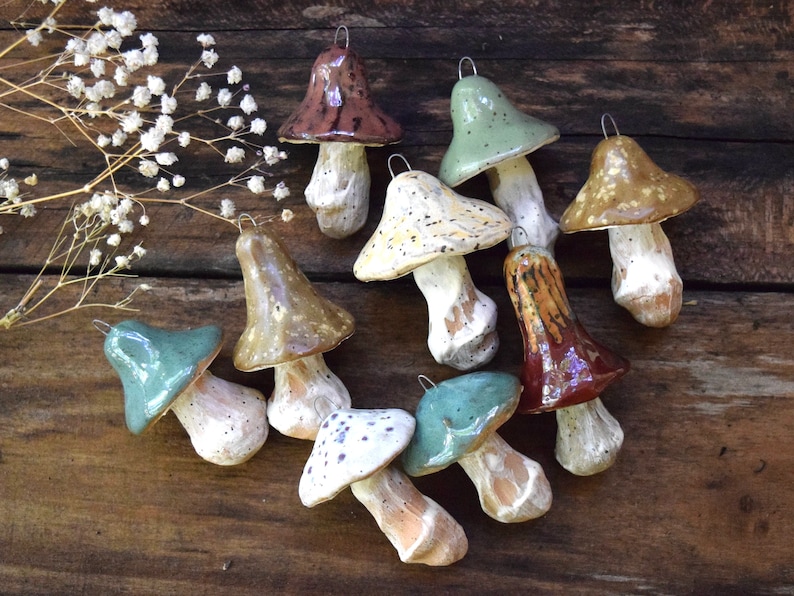 May include: A collection of ten ceramic mushroom ornaments in various colors and patterns, including brown, green, yellow, and white. The mushrooms are all hand-painted and have a rustic, vintage look.