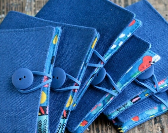 May include: A stack of six blue fabric pouches with colorful patterns on the inside. Each pouch has a blue button and a blue strap.