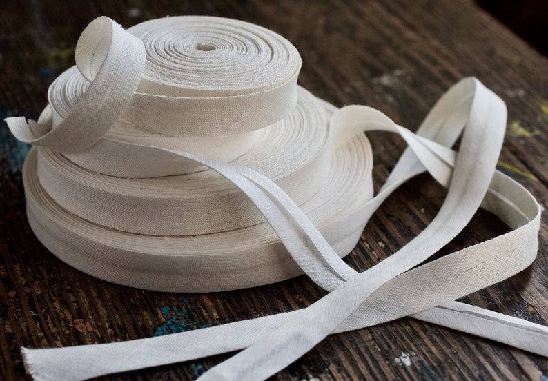 May include: A stack of white cotton twill tape, rolled and unrolled, on a wooden surface.