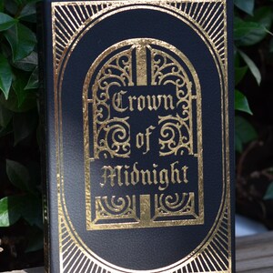 May include: A black book with a gold embossed design. The title is "Crown of Midnight" in a decorative font.