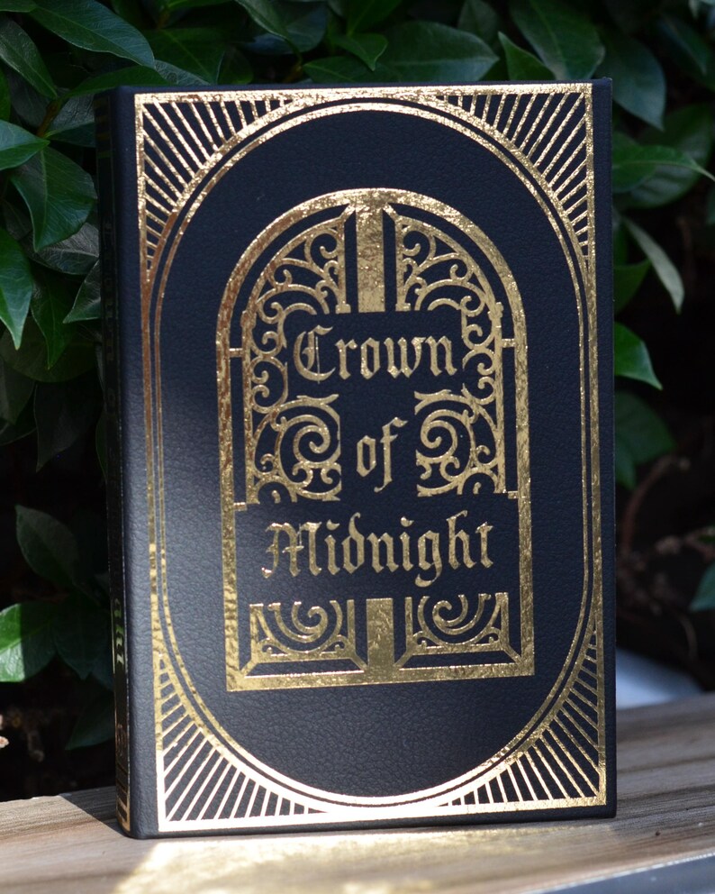 May include: A black book with a gold embossed design. The title is "Crown of Midnight" in a decorative font.