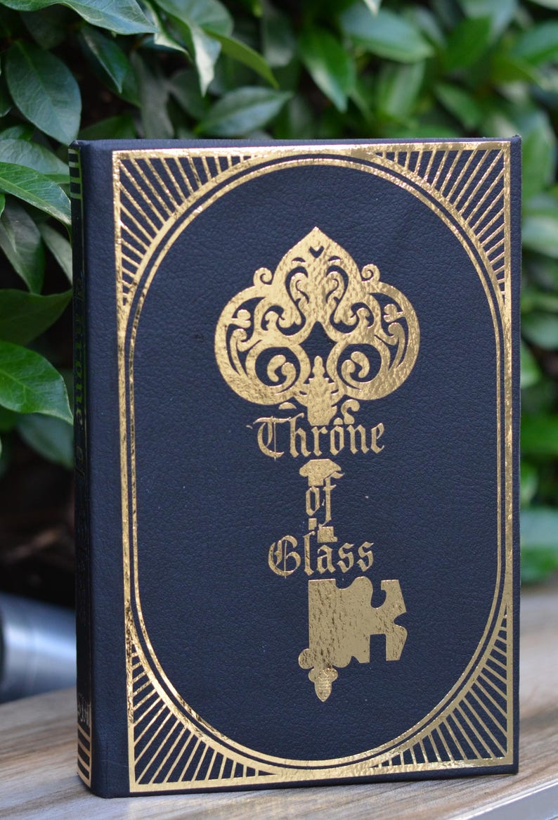 May include: A black book with a gold embossed design of a key with the words "Throne of Glass" on the cover.