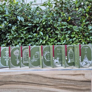 May include: A set of eight green hardcover books with silver and white illustrations and red ribbon bookmarks. The titles of the books are "The Assassin's Blade", "The Thief", "Crown of Midnight", "Queen of Shadows", "Heir of Fire", "Empire of Storms", "Tower of Dawn", and "Kingdom of Ash".