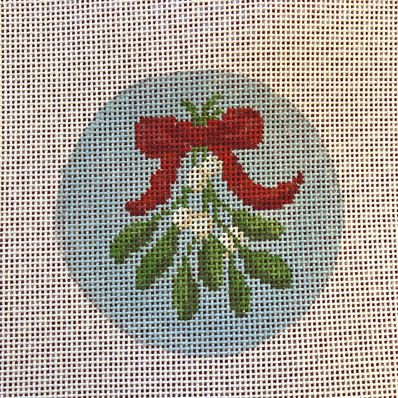 May include: Needlepoint design featuring a sprig of green mistletoe with white berries, a red bow, and green leaves. The design is set against a light blue background, perfect for holiday crafts.